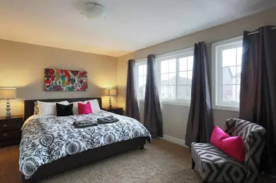 a bedroom with a bed and a chair and windows at Boardwalk Homes - Executive Townhomes in Kitchener