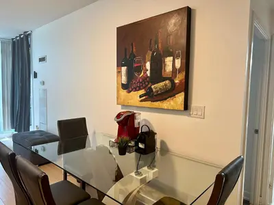 a dining room with a glass table and a painting of wine bottles at 1Bdrm plus den with 2 real beds plus sofabed & Terrace & parking in Toronto
