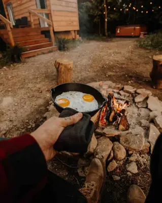 a person cooking eggs in a pan over a fire at The Green Acres Cabin in Hamilton