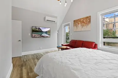a white bedroom with a bed and a red couch at ENTIRE BACHELOR UNIT EN-SUITE ACROSS FROM GOOGLE - br4 in Kitchener