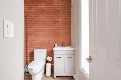 a bathroom with a white toilet and a brick wall at ENTIRE BACHELOR UNIT EN-SUITE ACROSS FROM GOOGLE - br3 in Kitchener