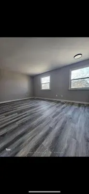 an empty living room with wood floors and two windows at Affordable Basment Apartment - London in London