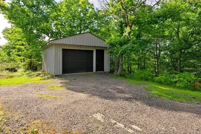 a garage with a gravel driveway in front of trees at Muskoka Retreat, Fire Pit, Games, Waterfront in Gravenhurst