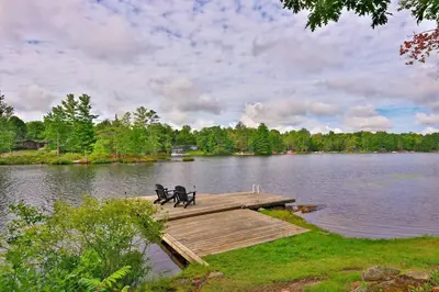 a wooden dock with two benches on a lake at Muskoka Retreat, Fire Pit, Games, Waterfront in Gravenhurst
