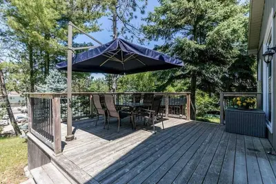 a wooden deck with a table and an umbrella at Cozy cottage on a private beach -Georgian Bay in Tiny
