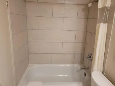 a white bath tub in a bathroom with white tiles at Sand Castle Suites Motel in Port Elgin