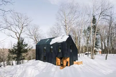a black barn with snow on top of a field at Camp Haliburton - Waterfront A-Frame in Wilberforce