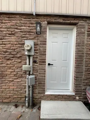 a door to a brick building with a meter next to it at Luxurious modern basement apartment in Pickering