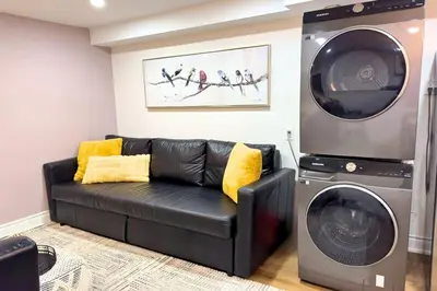 a living room with a black couch and a washing machine at Family-Friendly 2BR Ground-Level Suite with Full Kitchen, Parking and 20 Minutes to Downtown in Toronto