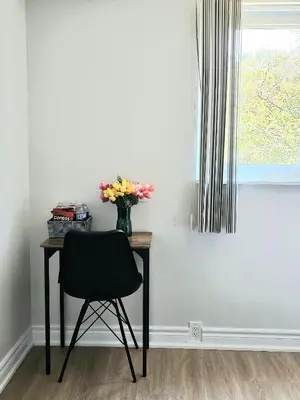 a table with a vase of flowers and a chair at A Home Away-Cozy Guest Room in Toronto in Toronto