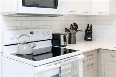 a white kitchen with a stove with a tea kettle at Casa Queen - Unique 2BR Suite in Leslieville in Toronto