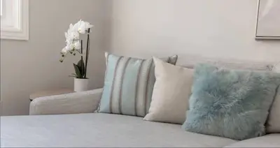 a couch with a pillow and a vase of flowers at Casa Queen East - Modern 2BR Suite in Leslieville in Toronto