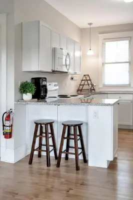 a kitchen with white cabinets and two bar stools at The Kiskadee - 49 Butternut in Cherry Valley