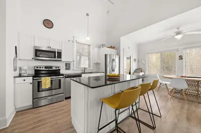 a kitchen with white cabinets and a counter with yellow chairs at L'Hibou - 18 Farm View in Cherry Valley