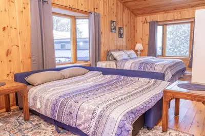 two beds in a room with wooden walls and windows at Lake View Loft in Severn