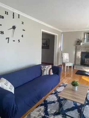 a blue couch in a living room with a clock on the wall at Cheerful 4 bedroom with sunroom in Belleville
