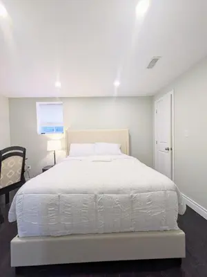 a white bedroom with a white bed and a chair at Kings Palace Basement in Brampton