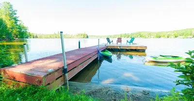 a dock with two chairs and a boat on a lake at Amazing Lakefront cottage on Paradise Lake in Haliburton