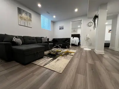 a living room with a black couch and wood floors at Cozy 2 Bedrooms Modern Basement Suite with Private entrance, Kitchen and parking in Mississauga