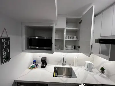 a white kitchen with a sink and a microwave at Cozy 2 Bedrooms Modern Basement Suite with Private entrance, Kitchen and parking in Mississauga