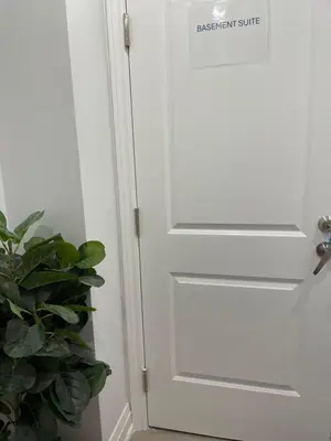 a white door with a sign on it next to a plant at Cozy 2 Bedrooms Modern Basement Suite with Private entrance, Kitchen and parking in Mississauga