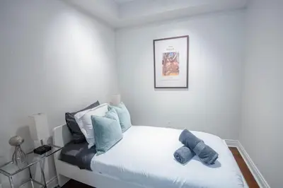 a white bedroom with a bed with blue pillows at 3BR Urban Gem with Scenic Balcony Views in Toronto