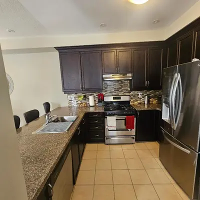 a kitchen with wooden cabinets and a stainless steel refrigerator at Exquisite Junior Bedroom in Brampton