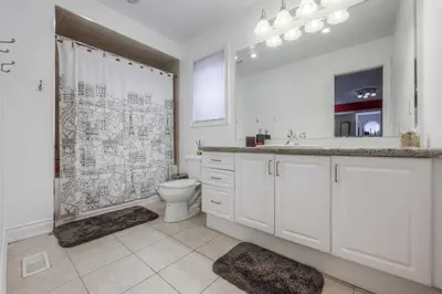 a white bathroom with a toilet and a shower at Connected Comfort - 7BR Family Retreat - Near Pearson Airport & Toronto Downtown in Brampton