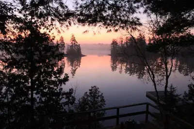 a view of a lake at sunset with trees at Private Lakefront Family Cottage with Tennis Court in Kinmount