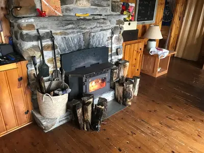 a stone fireplace in a living room with a stove at Private Lakefront Family Cottage with Tennis Court in Kinmount