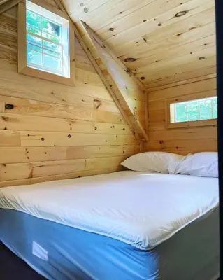 a bed in a log cabin with two windows at Wildwood Bunkies in Bailieboro