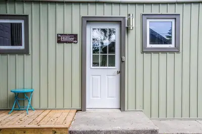 a green house with a white door and a blue stool at Westlake Cottage - Hillier Lodge in Wellington