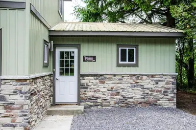 a green house with a stone wall and a white door at Westlake Picton Cottage in Wellington