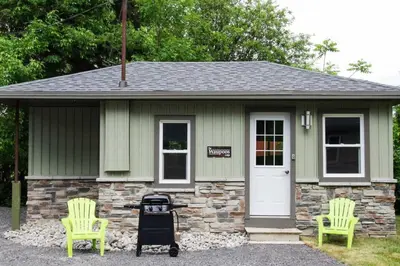a small house with two green chairs and a grill at Westlake Waupoos Cottage in Wellington