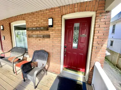 a red door on a brick house with two chairs at Entire guest suite in the Falls in Niagara Falls