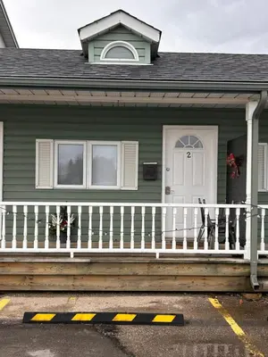 a green house with a white porch and a door at Smokehouse Suites and Stay in Guelph