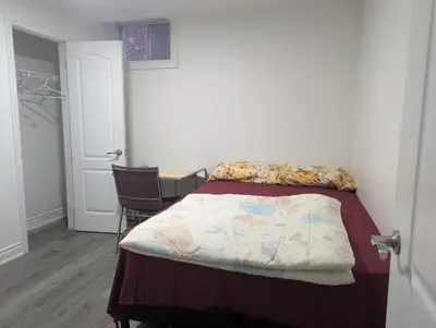 a small bedroom with a bed and a chair at Basement two Queen beds and one single with two full washrooms by YKF airport in Kitchener