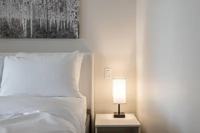 a bedroom with a white bed with a lamp on a table at Discounted Elegant Yorkville Suite in Toronto