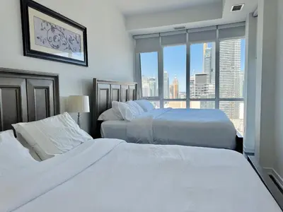 two beds in a bedroom with a view of a city at Two Storey Penthouse with 2 Parkings and Lake & City Views in Toronto