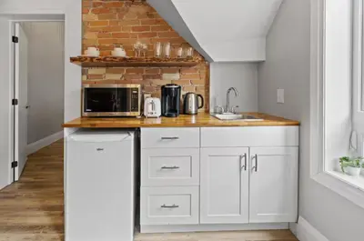 a kitchen with white cabinets and a brick wall at ENTIRE BACHELOR UNIT EN-SUITE ACROSS FROM GOOGLE - br2 in Kitchener