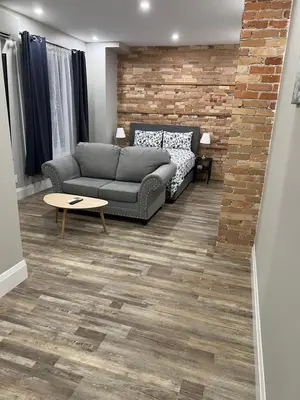a living room with a couch and a brick wall at ENTIRE BACHELOR UNIT EN-SUITE ACROSS FROM GOOGLE - br2 in Kitchener