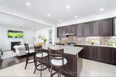 a kitchen with brown cabinets and a living room at Beautiful 4 bed, 3 master bedrooms-pvt washrooms in Brampton
