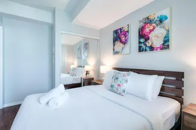 a white bedroom with two beds and a mirror at Panorama Luxe Suites - Prime Downtown Location in Toronto