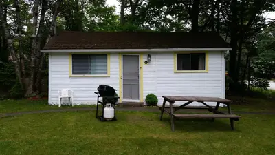 a small white house with a picnic table and a picnic table at Woodland Cedars Family Cottage Resort in Wasaga Beach