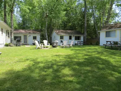 a yard with chairs and a grill and trees at Woodland Cedars Family Cottage Resort in Wasaga Beach