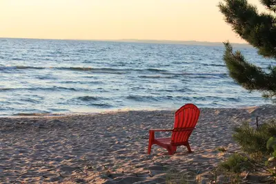 a red chair sitting on the beach near the ocean at Wymbolwood Lodge in Tiny