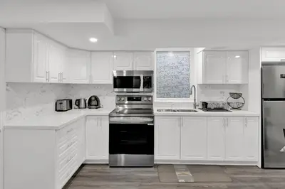 a white kitchen with stainless steel appliances and white cabinets at Cozy Ancaster Hamilton Apartment in Hamilton