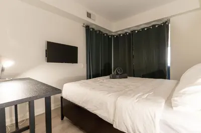 a bedroom with a white bed and a television at Chic 1BR plus Den Condo Near ROM and CN Tower in Toronto