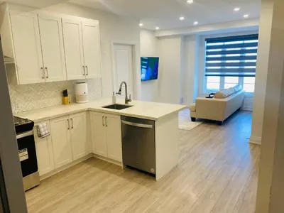 a kitchen with white cabinets and a sink and a living room at The Residence, Your comfort is our culture in Oakville