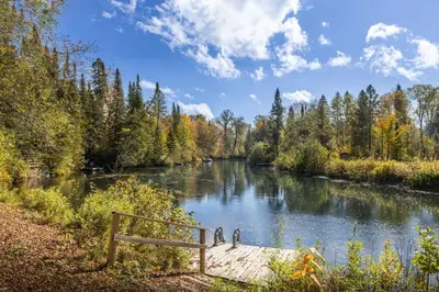 a bench sitting next to a river with trees at Hills Haven - Luxury Riverfront Cottage in Minden